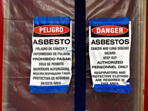 bilingual asbestos warning signs on plastic covering a front door