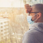 man wearing mask staring out office widnow