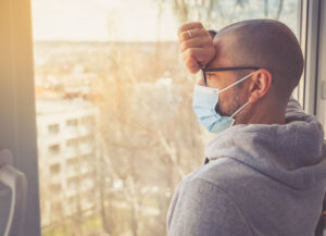 man wearing mask staring out office widnow